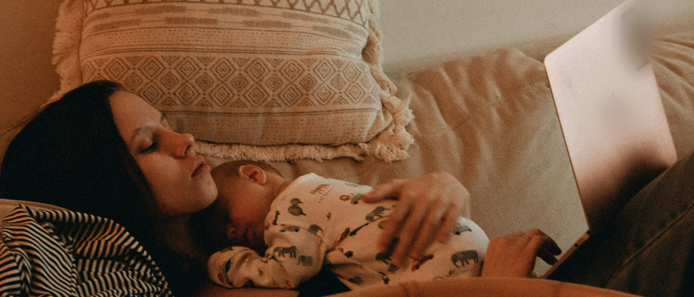 A mother resting with her newborn on her chest while working on a laptop